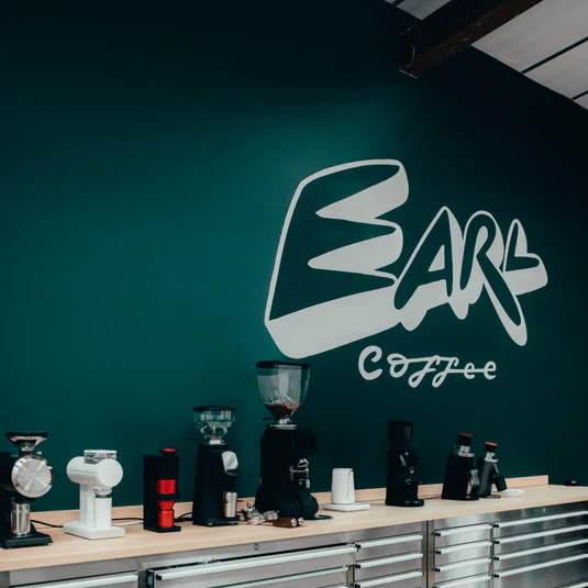 EARL Coffee showroom in Manchester with a row of espresso grinders along the counter and the painted EARL Coffee wordmark on the wall behind