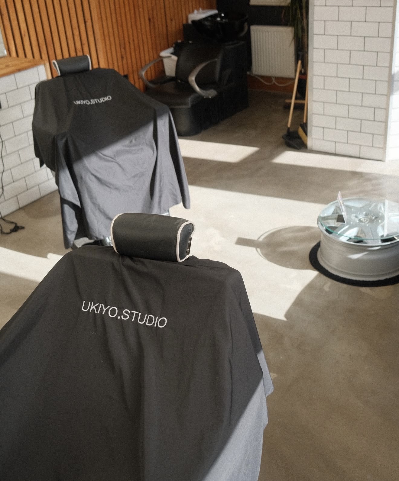 Two UKIYO.STUDIO branded barber capes draped over chairs by the wash station